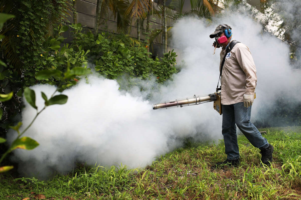 A mosquito control inspector wearing protective gear sprays a cloud of pesticide