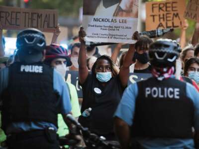 A protester holds a sign naming Nicholas Lee as a victim of Chicago policing during an outdoor demonstration