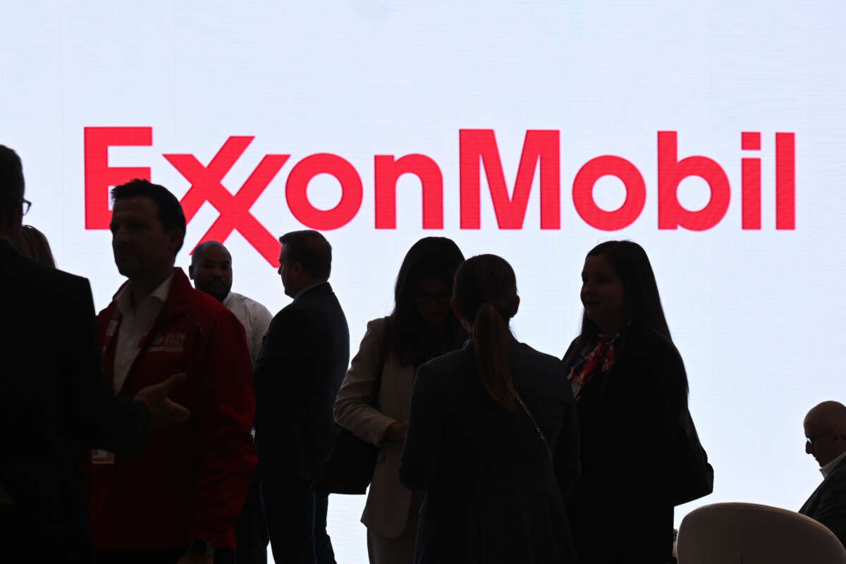 silhouettes of people walk in front of a bright ExxonMobil logo.