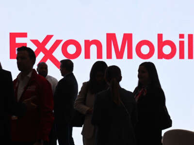 silhouettes of people walk in front of a bright ExxonMobil logo.