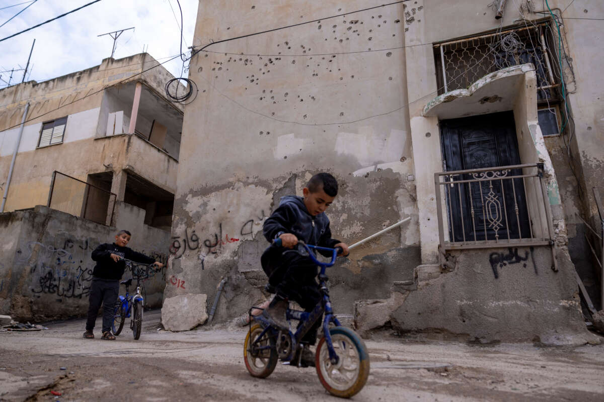 Kids ride bikes alongside a damaged building in Jenin refugee camp following days of Israeli raids, on December 31, 2023, in Jenin, West Bank.