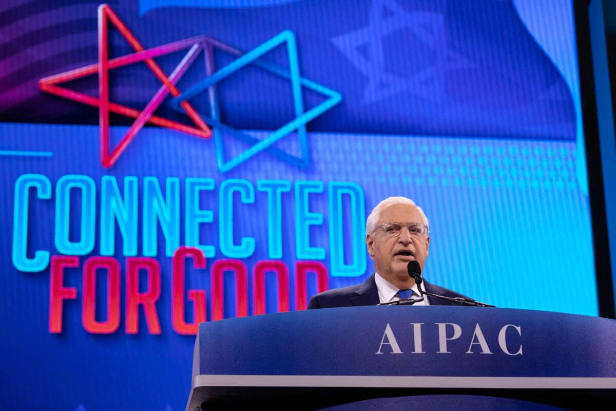 David Friedman speaks at a podium clearly labeled AIPAC with the words "CONNECTED FOR GOOD" alongside a 5-pointed star tangled with a Star of David behind him