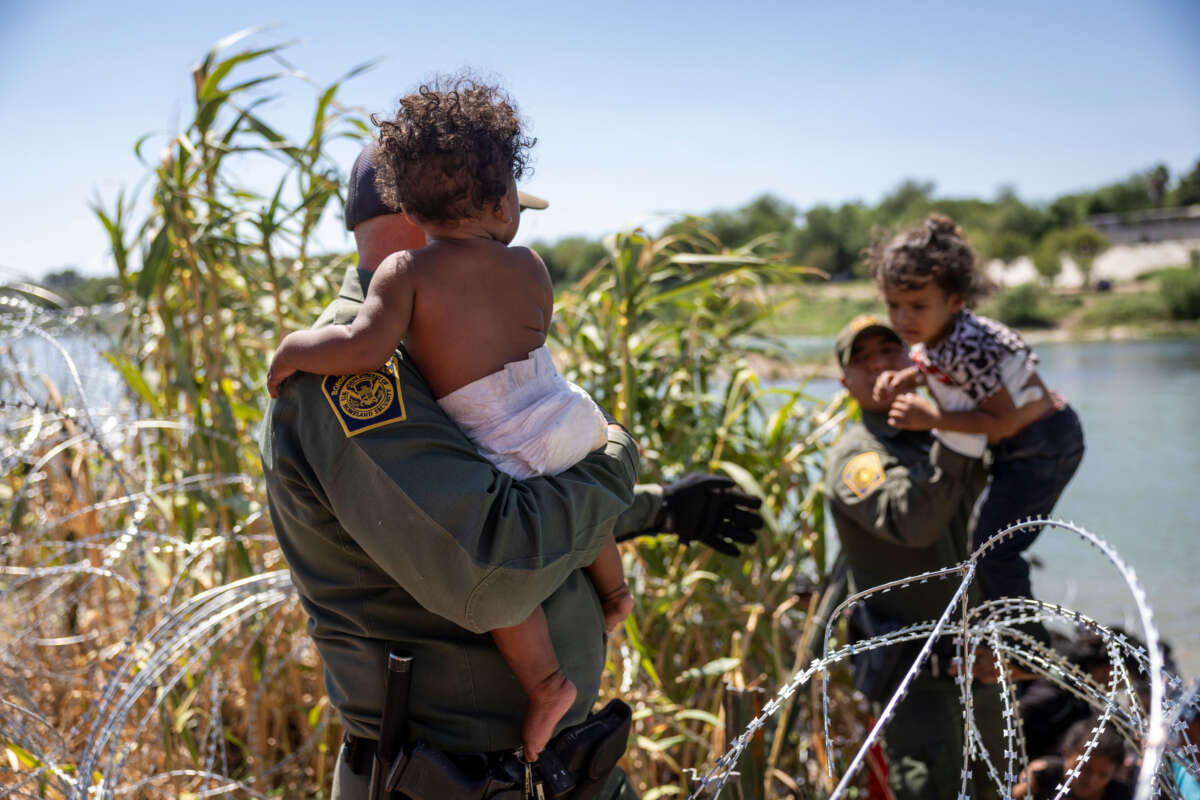 U.S. Border Patrol agents lift children through razor wire as families cross the Rio Grande from Mexico into the United States on September 28, 2023, in Eagle Pass, Texas.