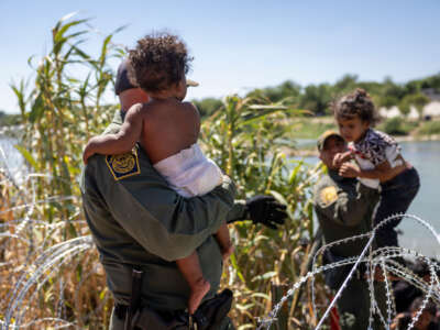 U.S. Border Patrol agents lift children through razor wire as families cross the Rio Grande from Mexico into the United States on September 28, 2023, in Eagle Pass, Texas.