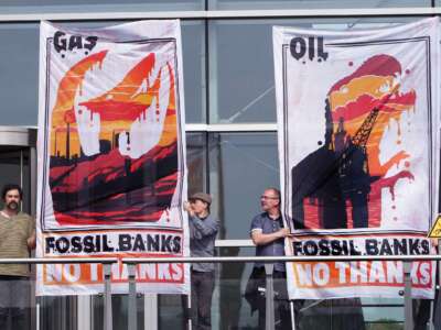 people hold signs reading "FOSSIL BANKS?NO THANKS" alongside images of the burning earth silhouetted in the shapes of dinosaurs
