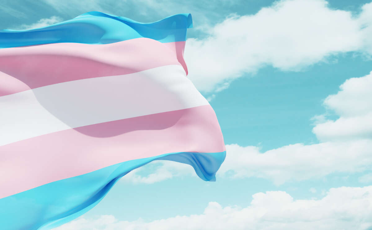 Transgender flag flying over blue cloudy sky