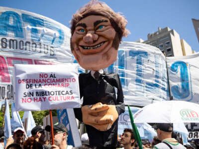 Protesters march with a large paper mache puppet of Argentine president Javier Milei