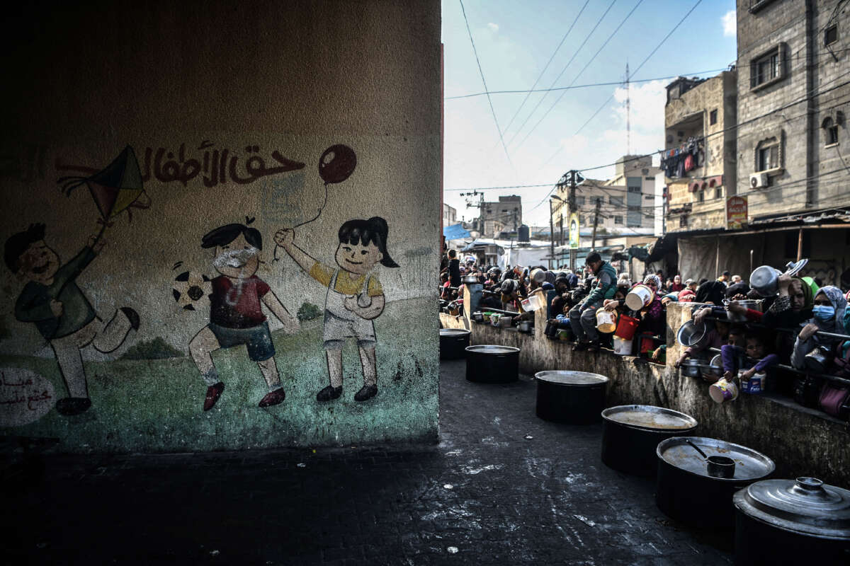 Palestinian people wait in queues with empty containers to get food distributed by charitable organizations as Israeli attacks continue in the city of Rafah, Gaza, on January 25, 2024.