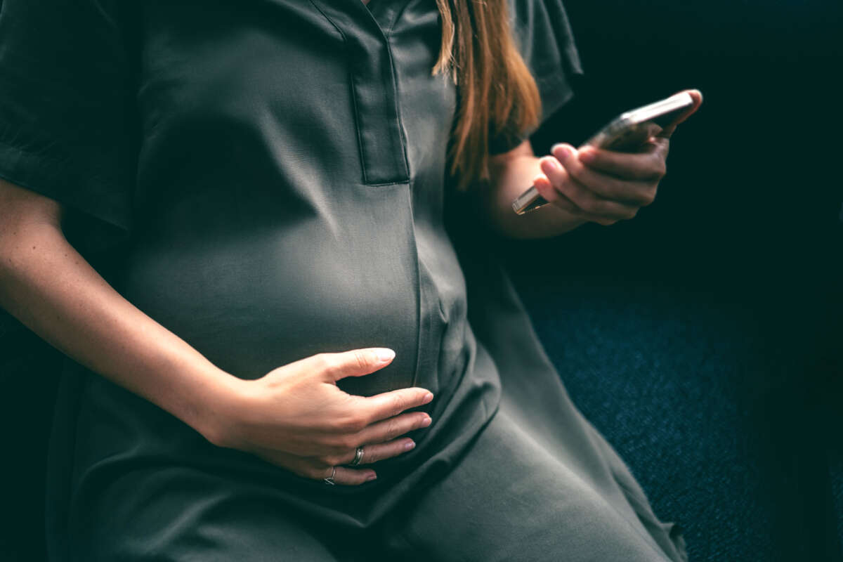 Pregnant person looks at cell phone while holding belly