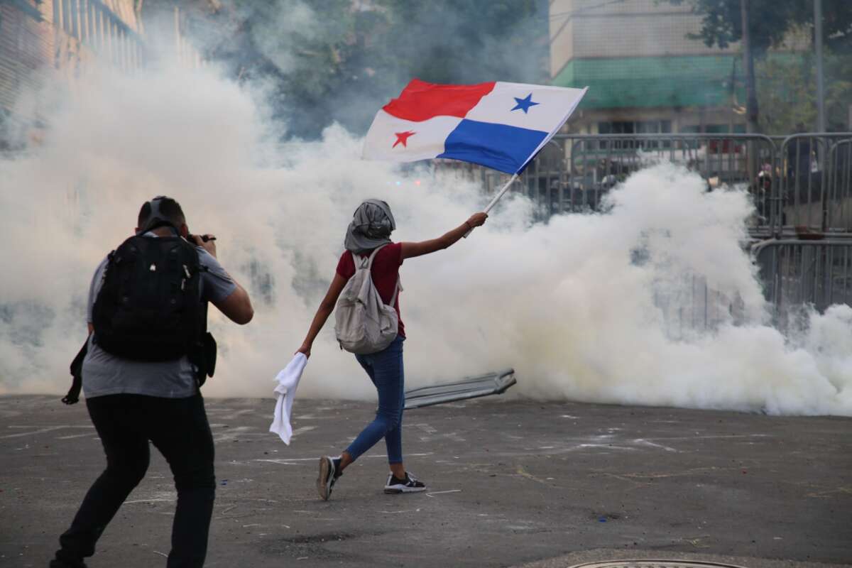 A protester waves Panama's flag as tear gas billows ahead.