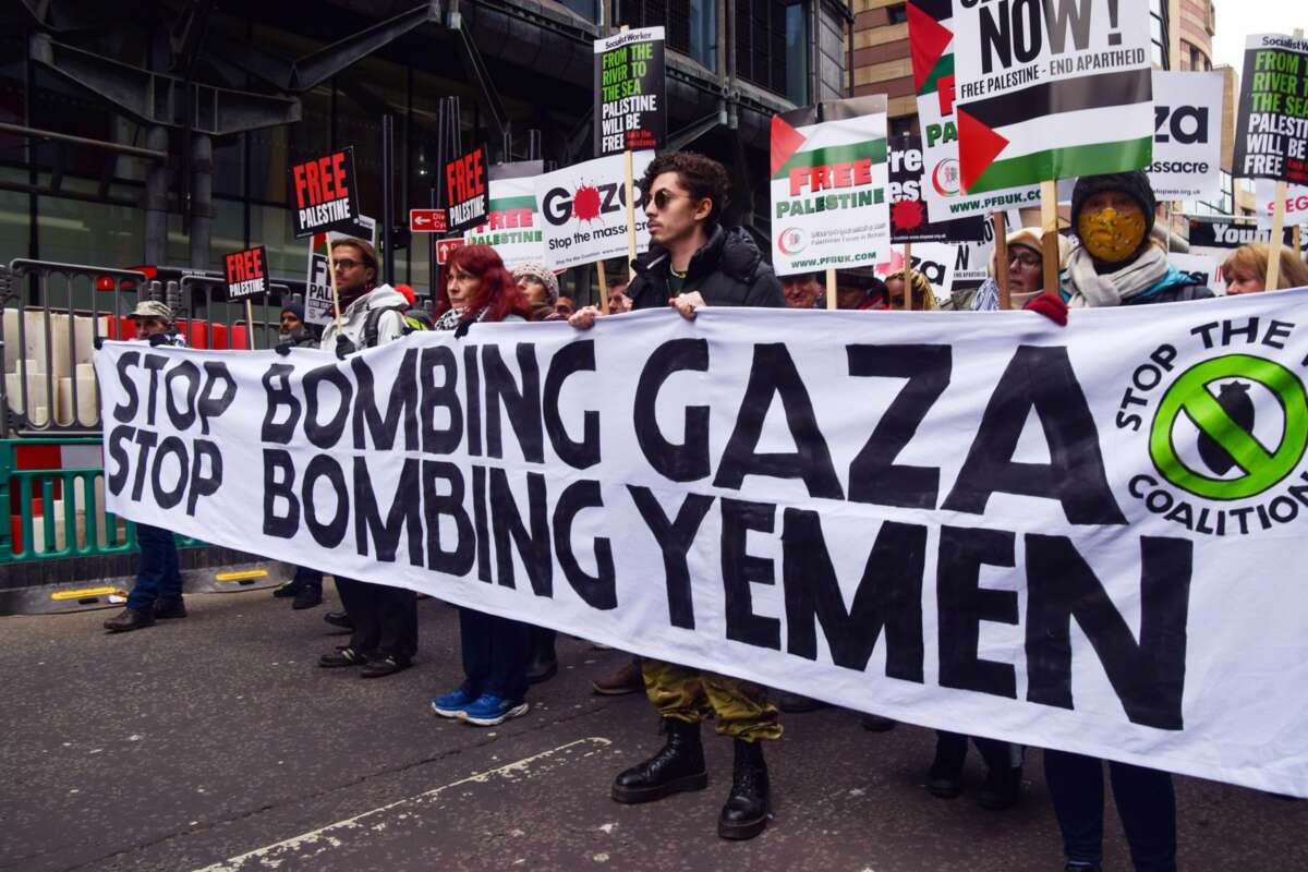 People march behind a banner reading "STOP BOMBING GAZA; STOP BOMBING YEMEN" during an outdoor protest