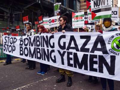 People march behind a banner reading "STOP BOMBING GAZA; STOP BOMBING YEMEN" during an outdoor protest
