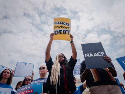 A Black woman holds a sign reading "CANCEL STUDENT DEBT" during an outdoor protest