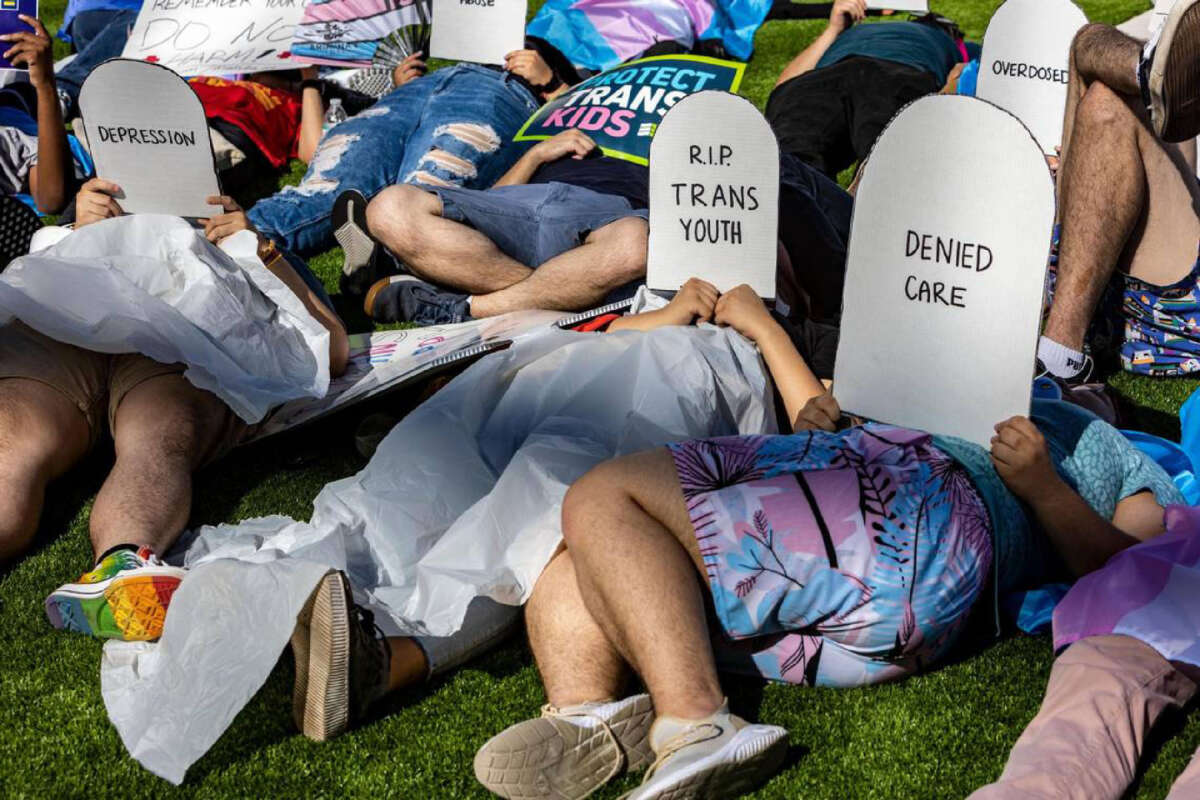 Protesters lie on the ground holding cardboard signs shaped like tombstones in front of the Marriott Fort Lauderdale Airport as the Florida Board of Medicine meets inside, on August 2, 2023.
