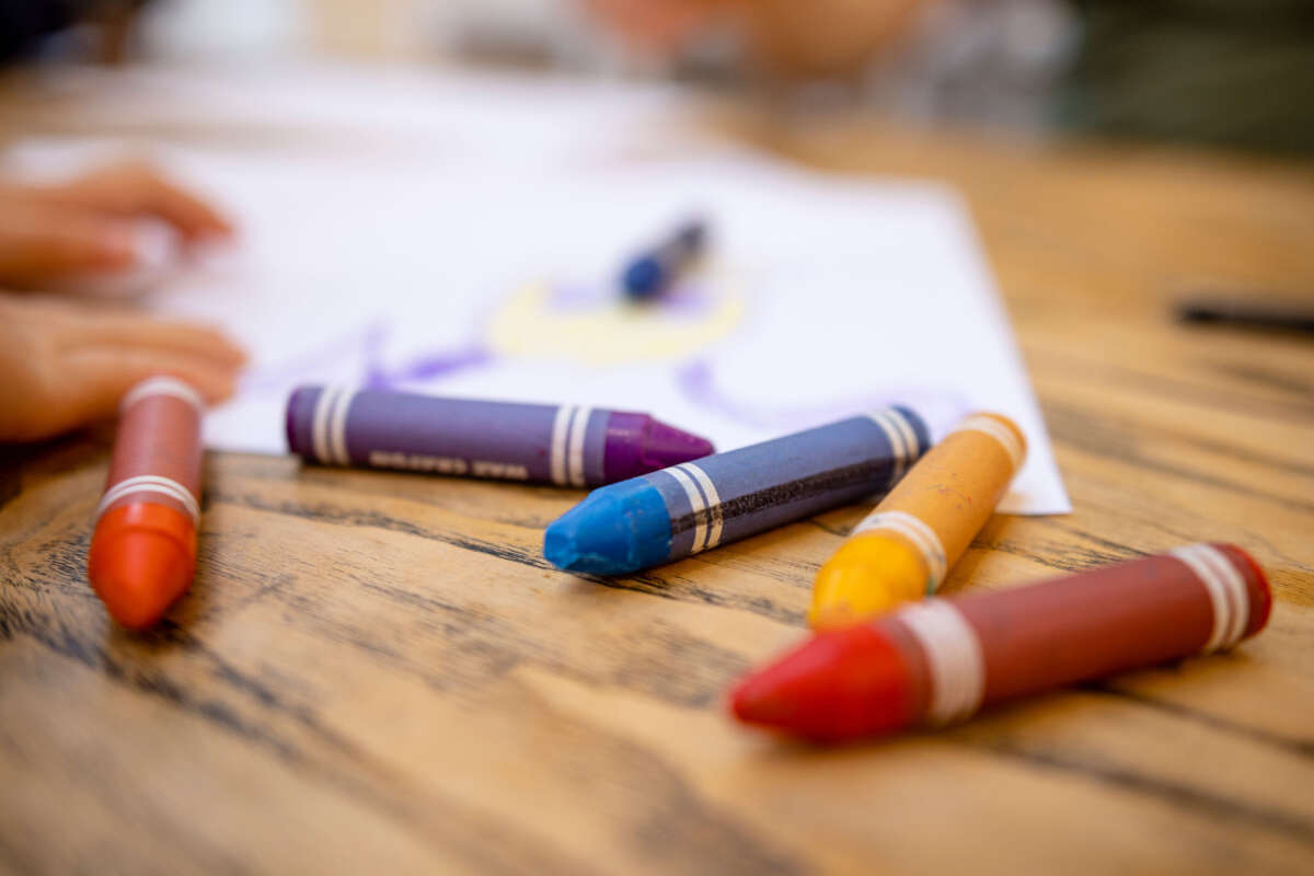 A close-up shot of colorful crayons on a wooden table with paper.