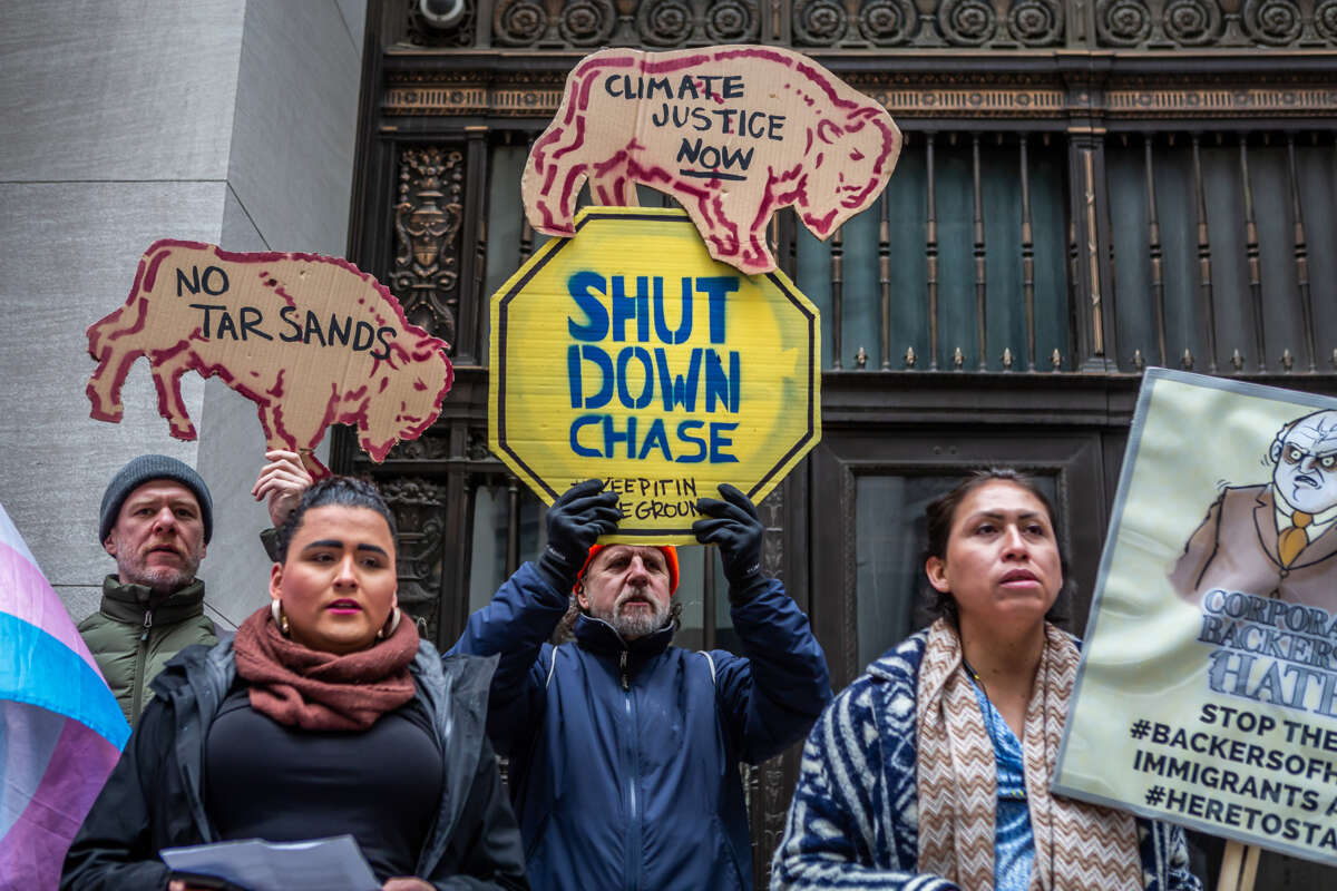 People display signs reading "SHUT DOWN CHASE" and "CLIMATE JUSTICE NOW" during an outdoor demonstration