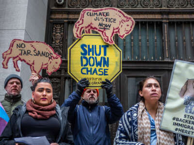 People display signs reading "SHUT DOWN CHASE" and "CLIMATE JUSTICE NOW" during an outdoor demonstration