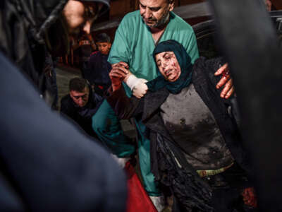 A bloodied woman is escorted into a hospital by a doctor