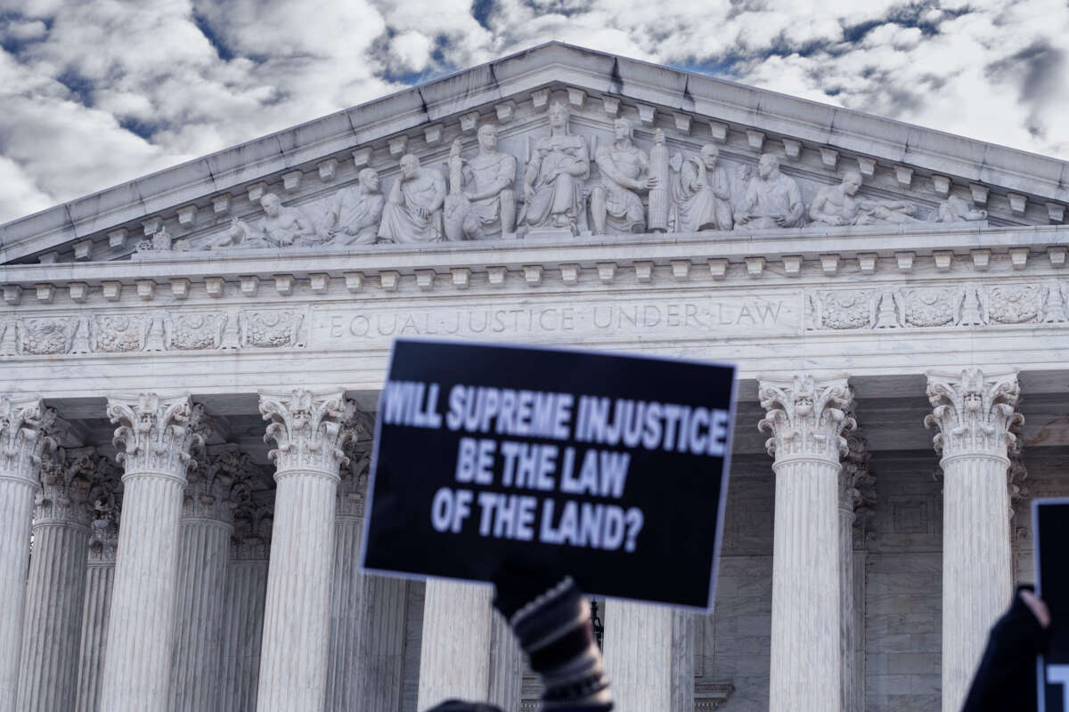 A person holds a sign reading "WILL SUPREME INJUSTICE BE THE LAW OF THE LAND?" during a protest on the steps of the US Supreme Court building