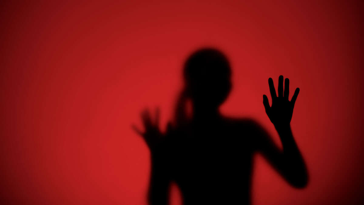 A woman's silhoutte is seen against a red background with hand in sharp focus
