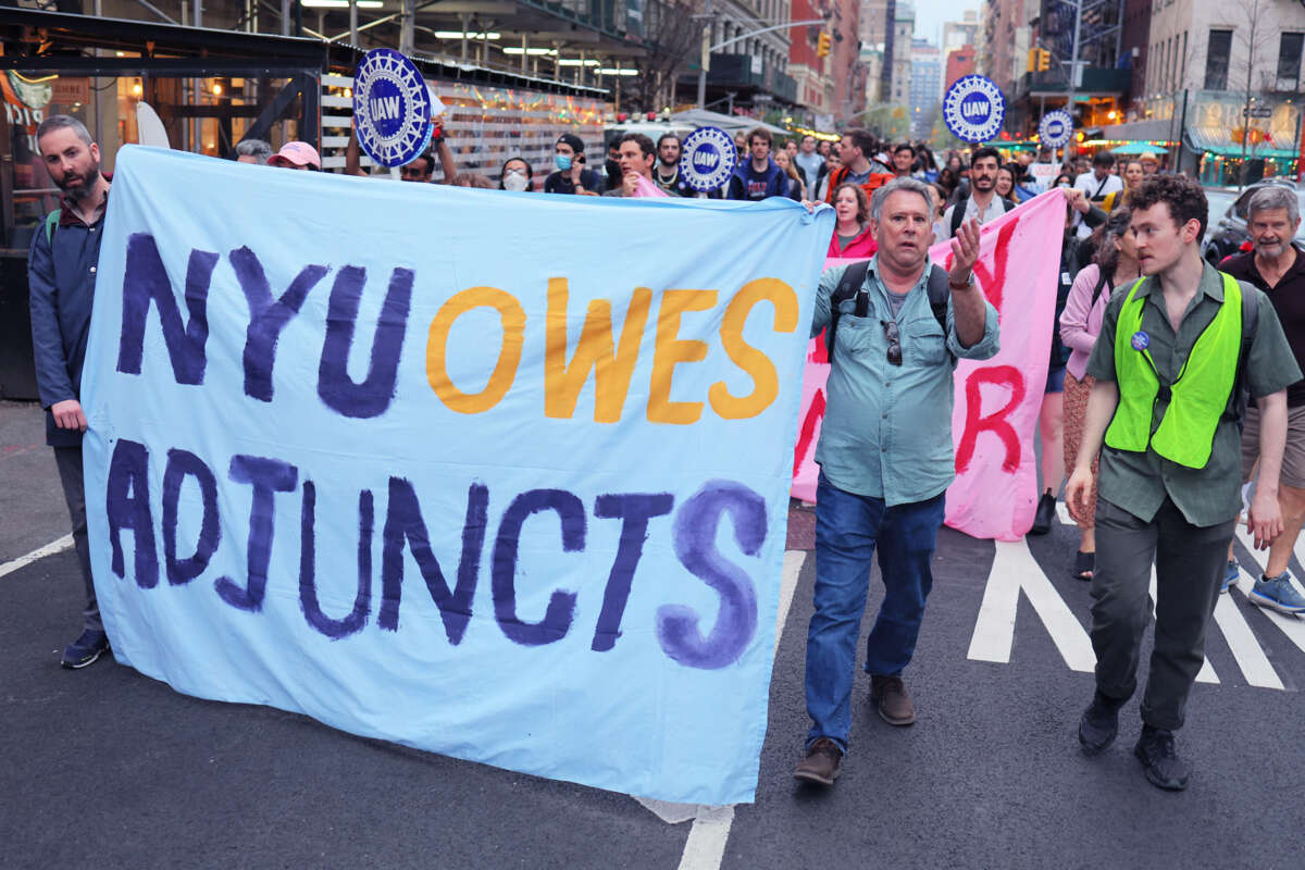 People march behind a banner reading "NYU OWES ADJUNCTS" during an outdoor protest