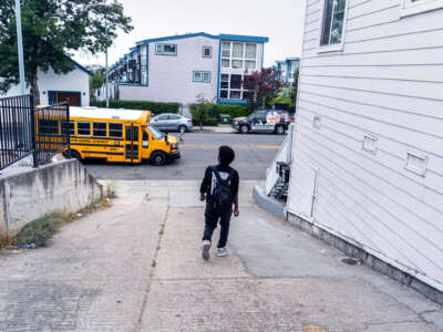 A student walks to the yellow school bus waiting for him at the end of his driveway