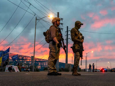 As a man sells Trump flags on the left, gun-carrying Trump supporters stand against the backdrop of a dusk sky during a gathering of pro-Trump supporters outside the Maricopa County elections building to protest election results on November 6, 2020, in Phoenix, Arizona.