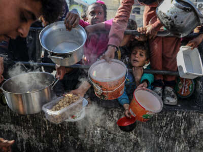 Palestinian children wait in line to receive food prepared by volunteers for Palestinian families displaced to Southern Gaza due to Israeli attacks, between rubble of destroyed buildings in Rafah, Gaza, on February 9, 2024.