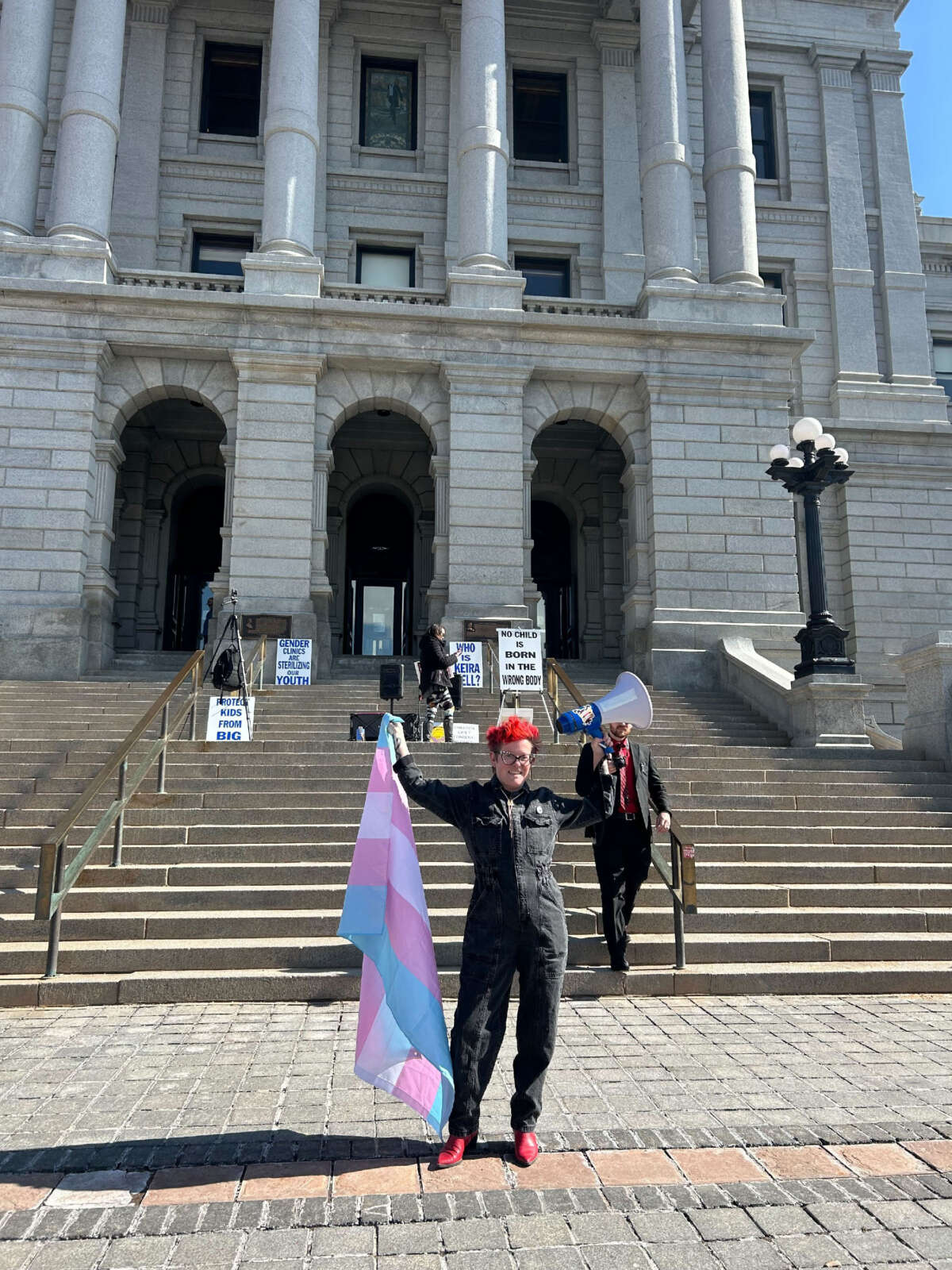 A pro-trans activist stands in front of an anti-trans demonstration.