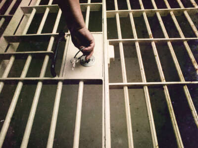 A hand with keys unlocks a prison cell door.