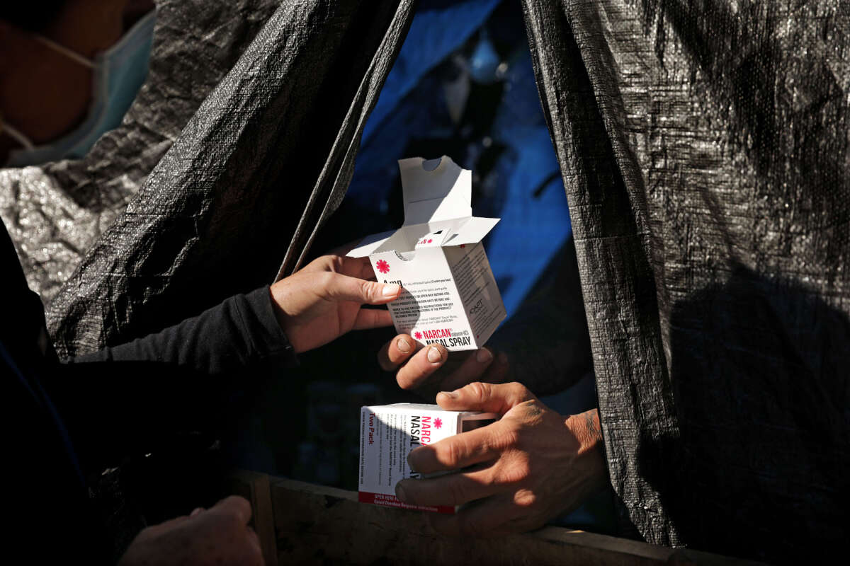 Hand of a nurse passes a box of Narcan to an unhoused person in a tent in Los Angeles