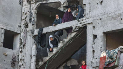 Palestinian women and children look on as they stand at the structure of a heavily damaged building on February 22, 2024, following overnight Israeli air strikes in Rafah refugee camp in the southern Gaza Strip.