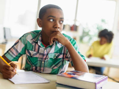 Black student sits at desk with pencil, notebook and textbook in class