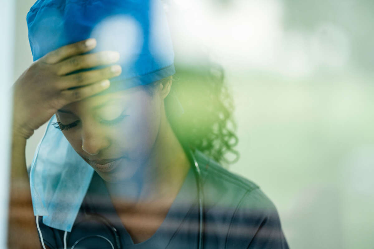 A Black health care worker appears tired through a window