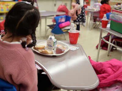 A tiny girl in a tiny chair eats a tiny breakfast with the rest of her tiny kindergarten class