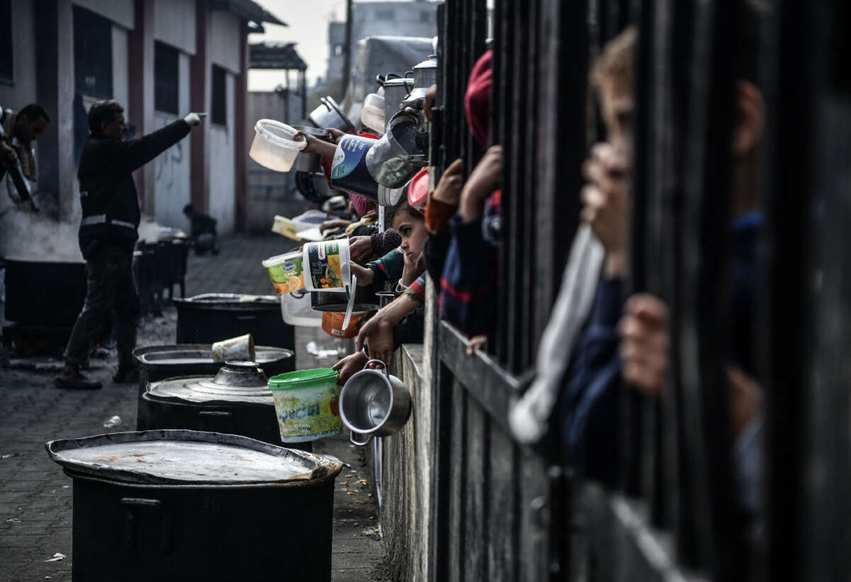 Palestinians hold out their empty containers to be filled with food, distributed by charity organizations, behind bars since they are unable to obtain basic food supplies due to the embargo imposed by Israeli forces in Rafah, Gaza, on February 25, 2024.