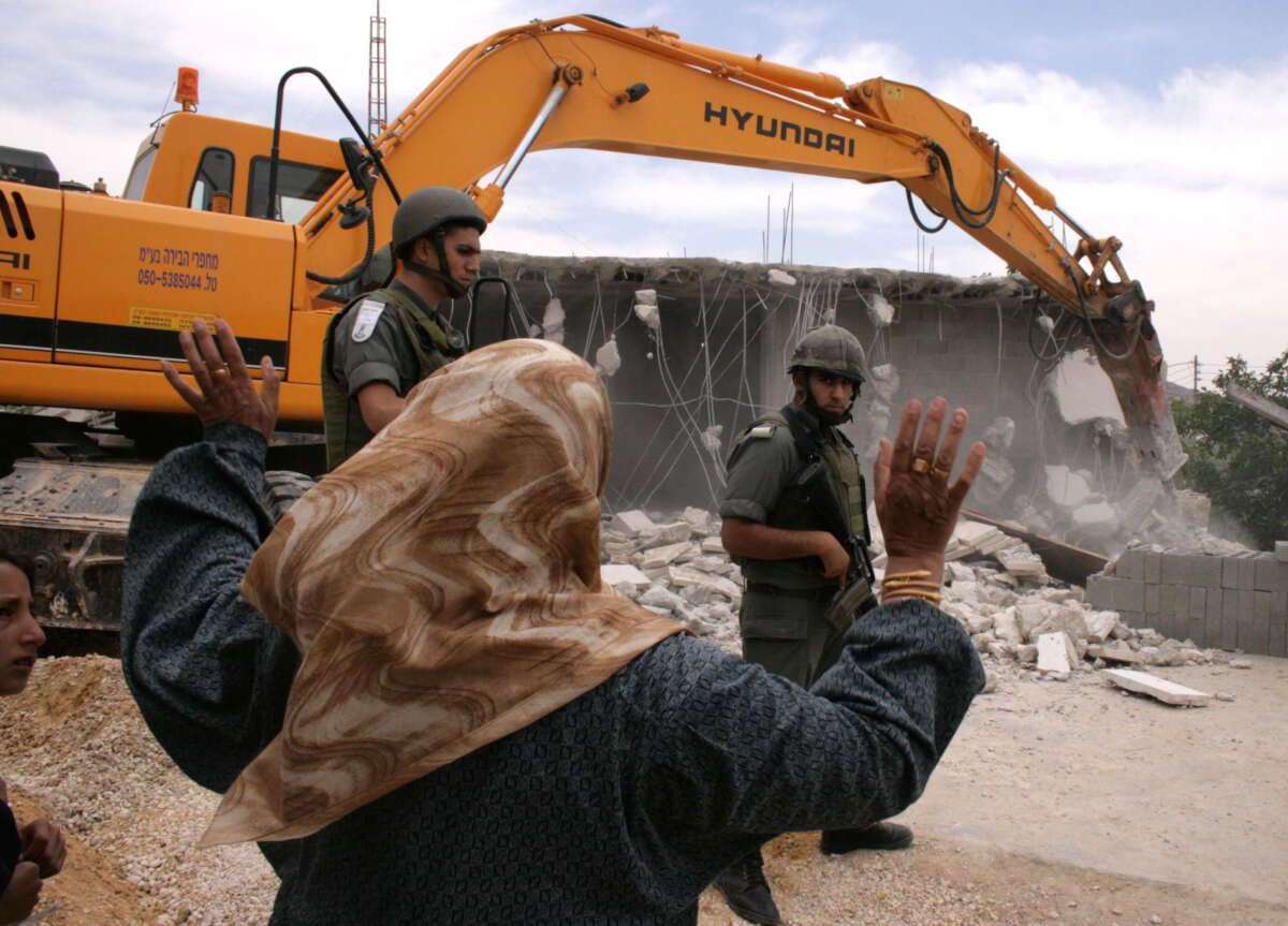 A Palestinian woman shouts at Israeli soldiers as they guard a bulldozer that is destroying her home