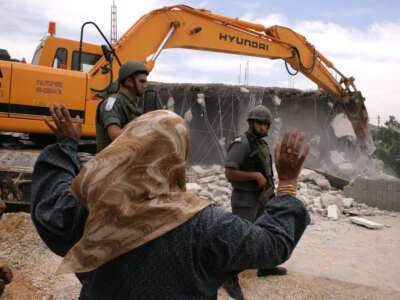 A Palestinian woman shouts at Israeli soldiers as they guard a bulldozer that is destroying her home