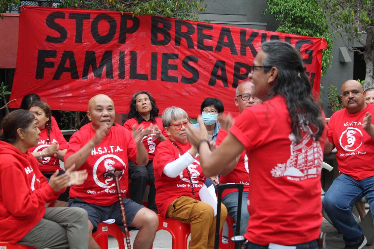 Members of the Hillside Villa Tenants Association clap and chant in front of a banner which says "Stop Breaking Families Apart."