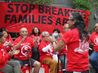 Members of the Hillside Villa Tenants Association clap and chant in front of a banner which says "Stop Breaking Families Apart."