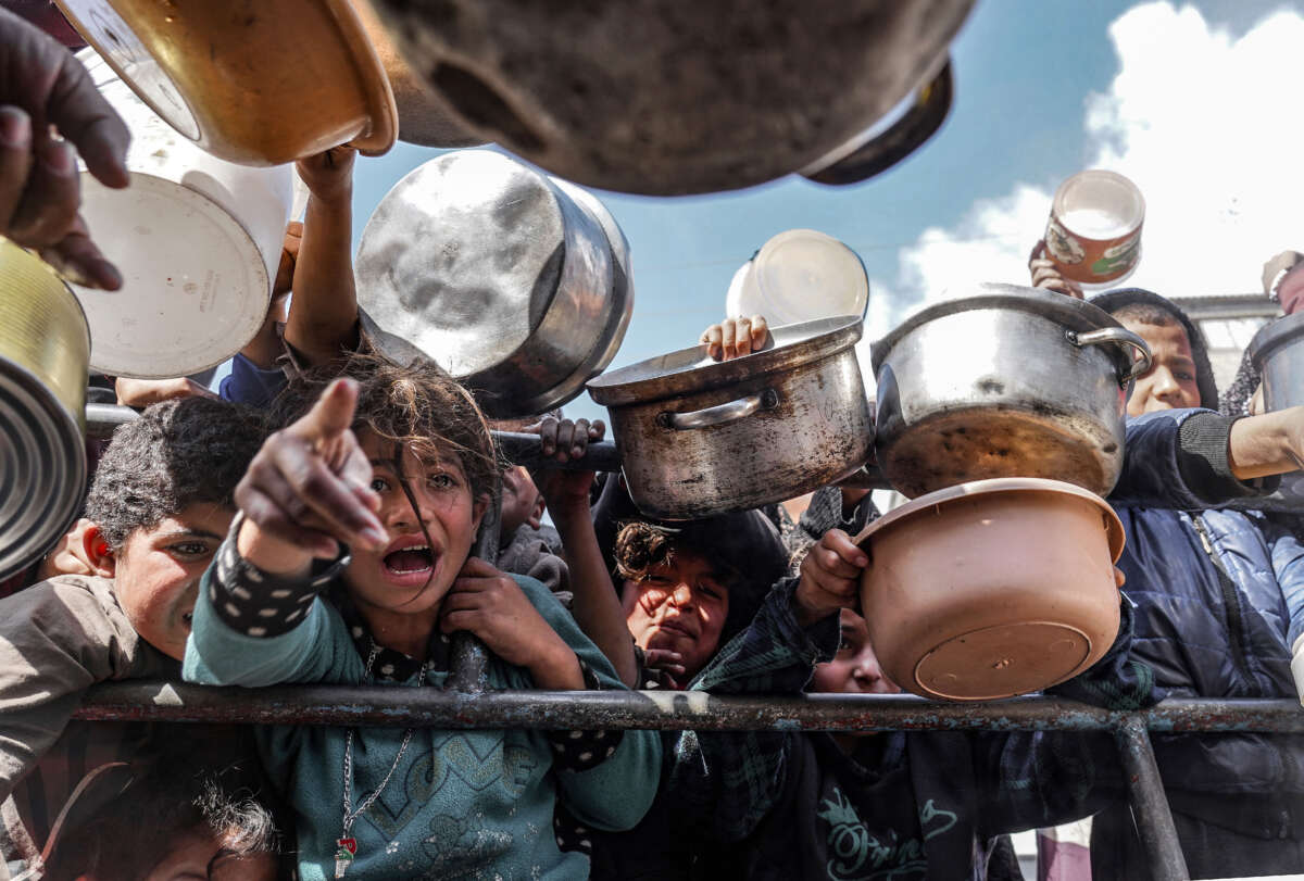 Palestinian children, holding empty pots, wait in line to receive food prepared by volunteers for Palestinian families displaced to Southern Gaza due to Israeli attacks, in Rafah, Gaza, on February 10, 2024.