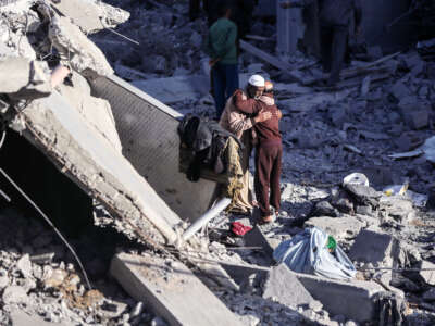 Two Palestinian men embrace among the rubble of their homes