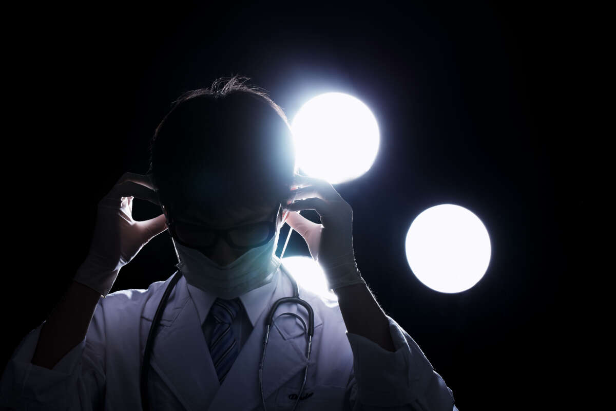 A doctor wear a mask is backlit by two bright white lights in a dark space