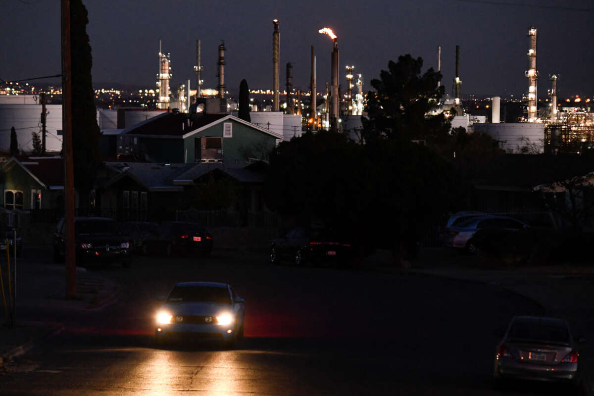 A vehicle drives through a neighborhood as a flaring tower and storage tanks stand on the horizon at the Marathon Petroleum Corp. El Paso oil refinery on December 10, 2021, in El Paso, Texas.