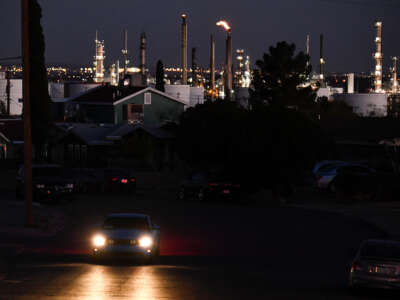 A vehicle drives through a neighborhood as a flaring tower and storage tanks stand on the horizon at the Marathon Petroleum Corp. El Paso oil refinery on December 10, 2021, in El Paso, Texas.