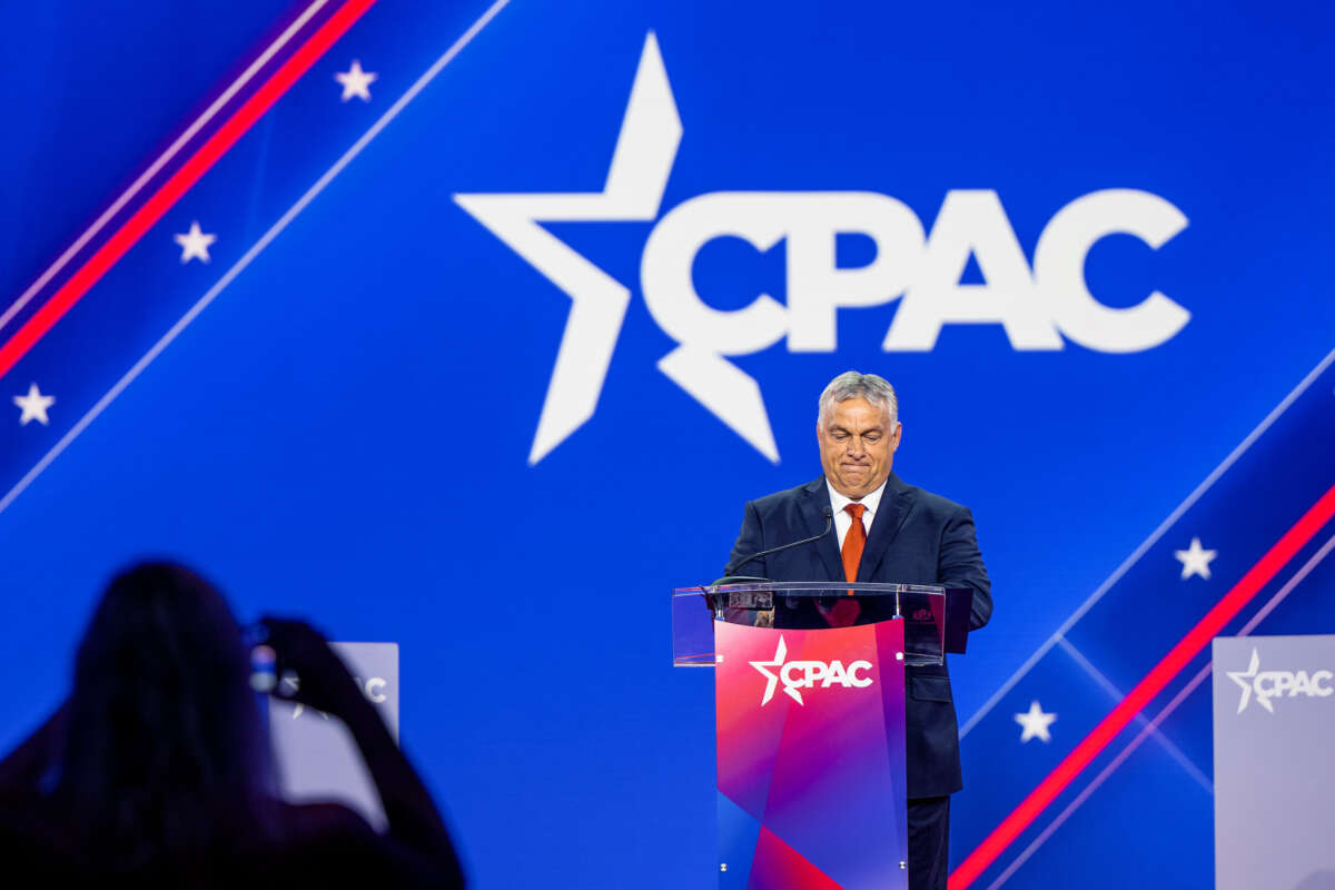 Viktor Orban stands behind a podium with an enormous CPAC logo behind him