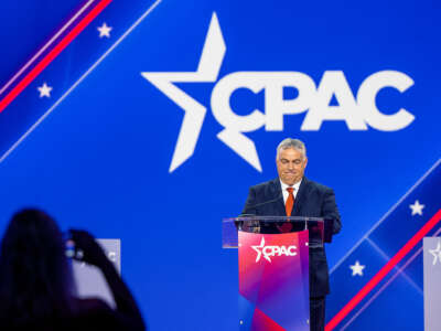 Viktor Orban stands behind a podium with an enormous CPAC logo behind him