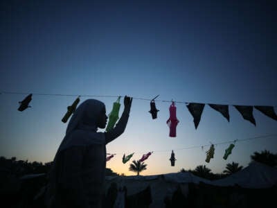 A hijabi strings unlit paper lanterns onto a rope as the sun sets behind her