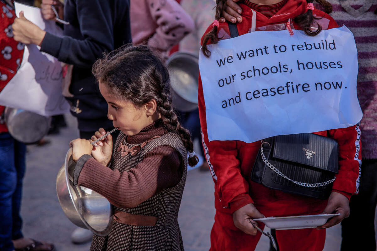 A child holds an empty bowl as another holds a sign reading "We want to rebuild our schools, houses; ceasefire now"