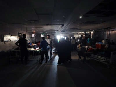 Doctors treat their patients in a darkened hospital room lit only by the daylight coming in from an open door